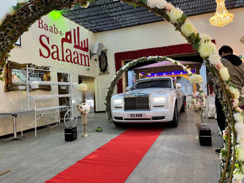 White Rolls-Royce entering Baab-e-Salaam Banqueting Hall White Rolls-Royce entering Baab-e-Salaam Banqueting Hall on red carpet under floral arches