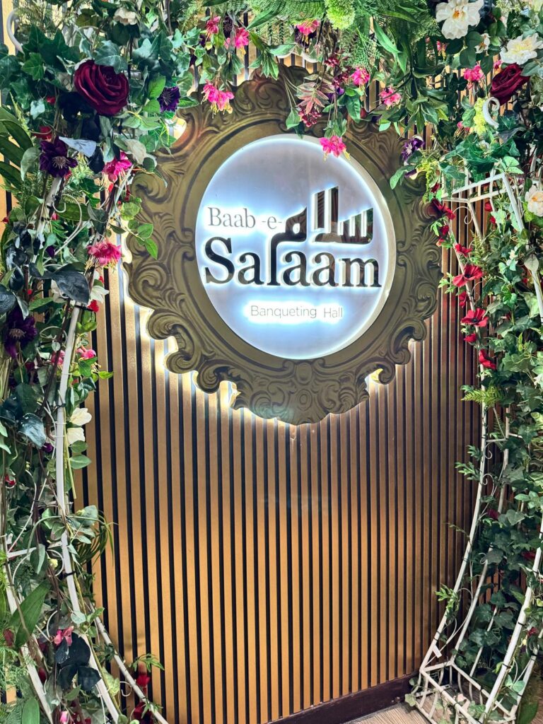 Baab-e-Salaam Banqueting Hall illuminated sign surrounded by floral arch decor