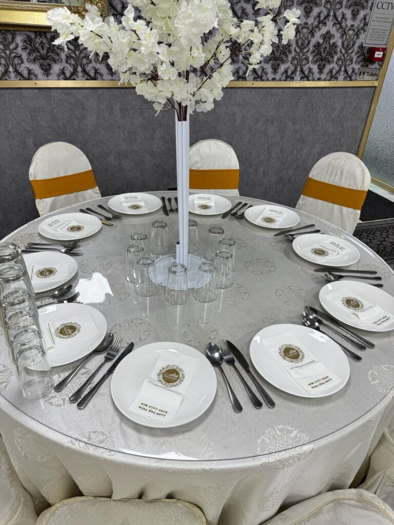 Elegant round table setup with white floral centerpiece and branded napkins at Baab-e-Salaam Banqueting Hall